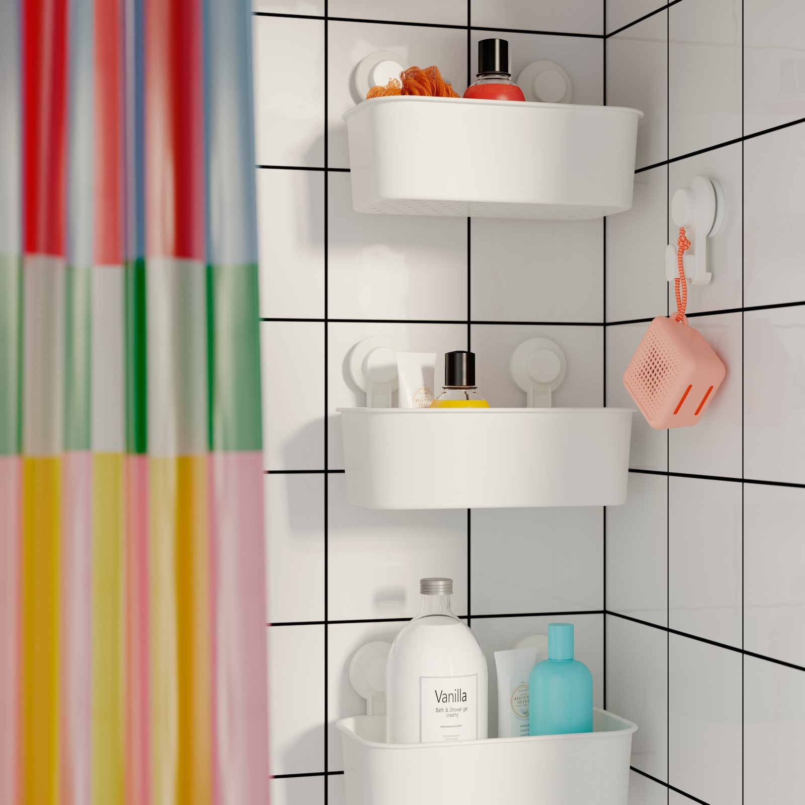 Three TISKEN baskets with suction cups hanging vertically in a row near a colourful shower curtain and a pink WiFi speaker.