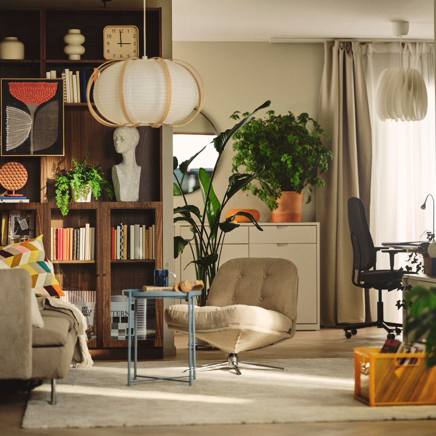 A living room features a brown BILLY bookcase with a walnut effect, filled with books beside plants and a soft chair.