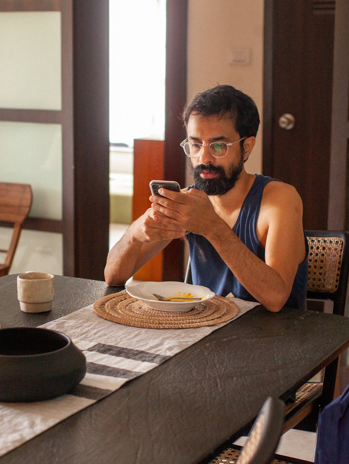 Man eating breakfast, looking at his phone in a calm dining room.