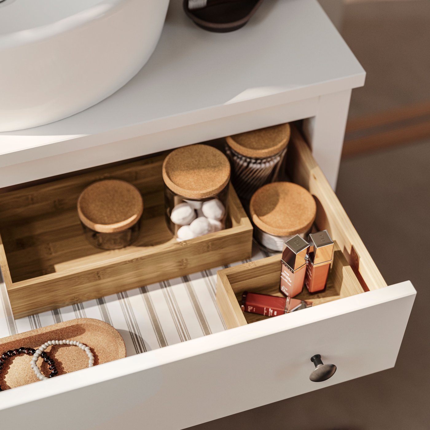 A white HEMNES washstand has an open drawer and inside are glass jars with cork lids and TAVELÅN trays with care products.