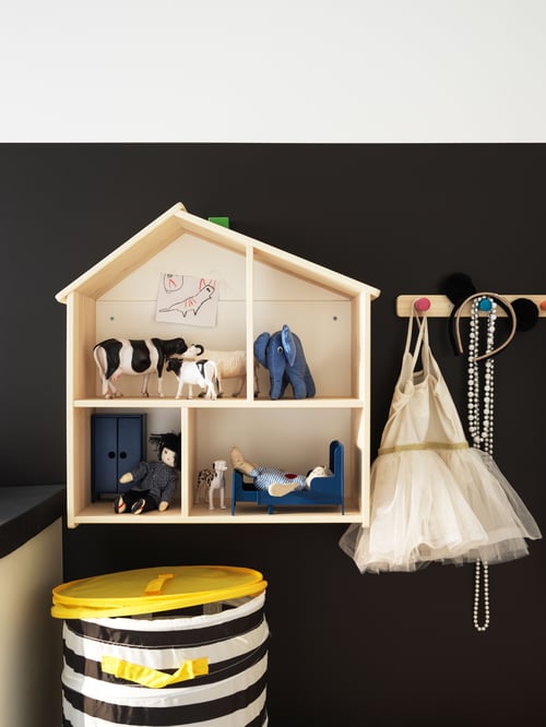 Kinderzimmer mit schwarzer Wand, hölzernem Puppenhaus und Wandregal, gestreiftem Korb mit gelbem Deckel und Holzgriff.