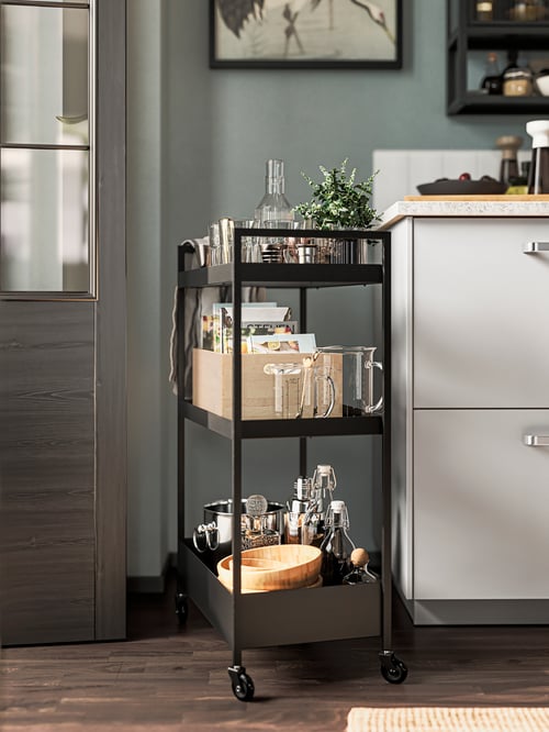 A modern kitchen with a NISSAFORS trolley filled with kitchen items, including a serving bowl, and placed beside a cabinet.