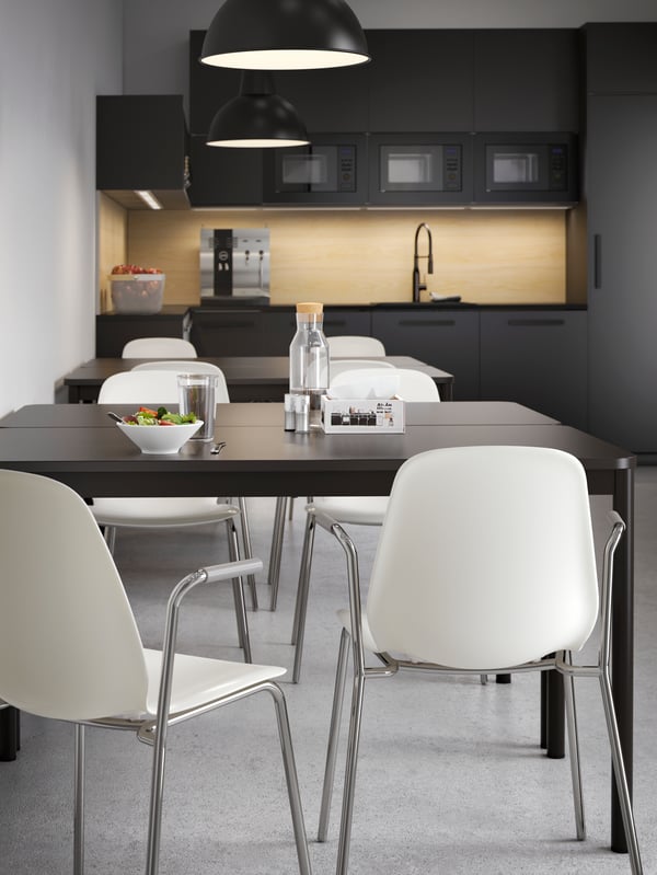 Two groups of kitchen tables in dark brown with white chairs, in a kitchen with dark fronts and a clean look.