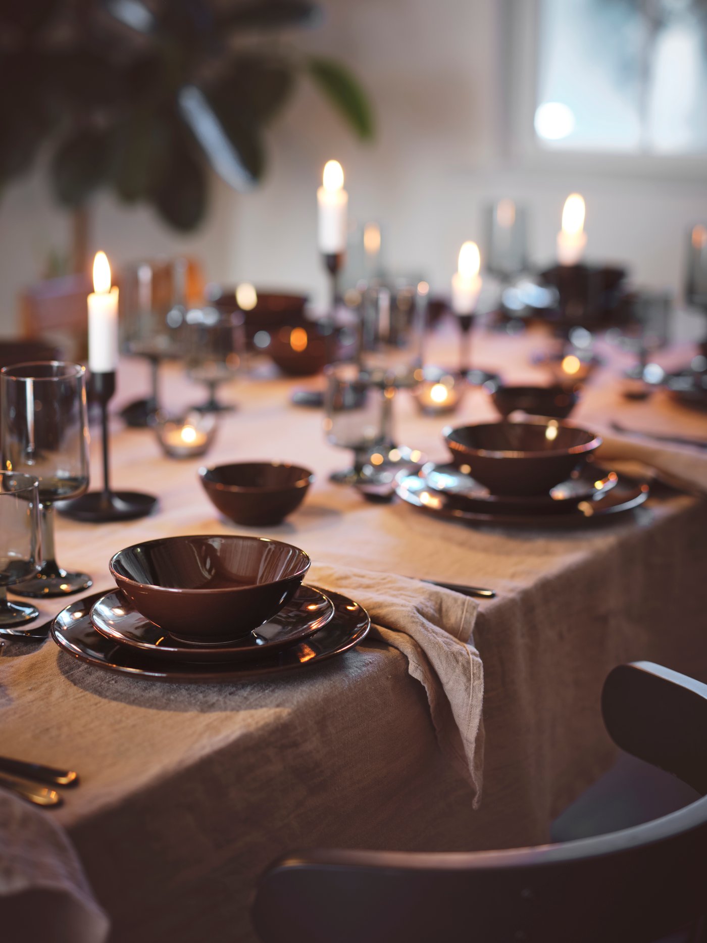 Zona de comedor con varios cuencos marrones en platos pequeños, copas de vino y portavelas. Todo se encuentra sobre una mesa.