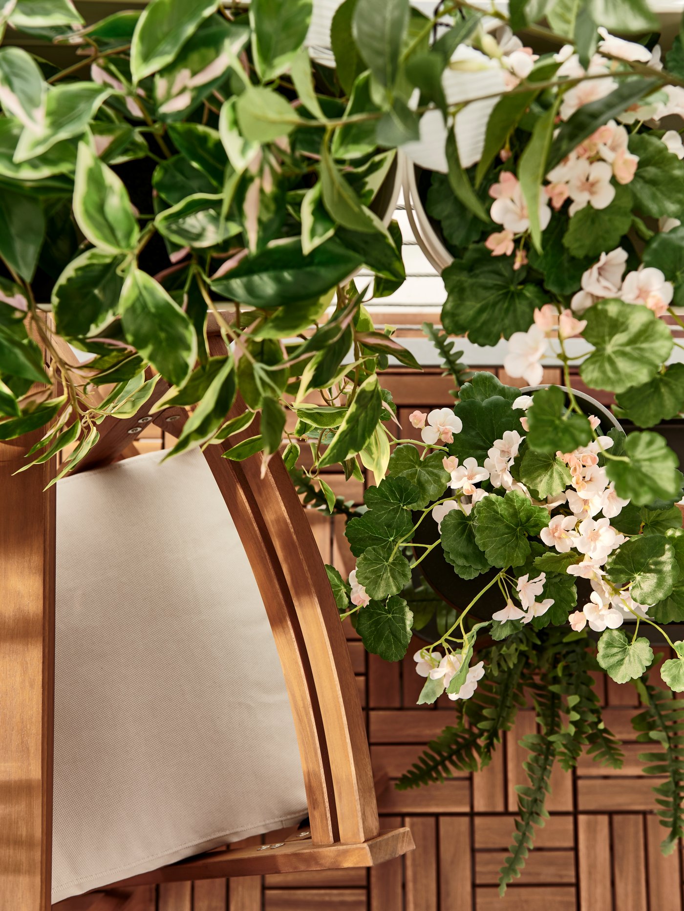 Sedia pieghevole NÄMMARÖ in legno chiaro su pavimento per esterni, accanto a piante verdi e fiori.