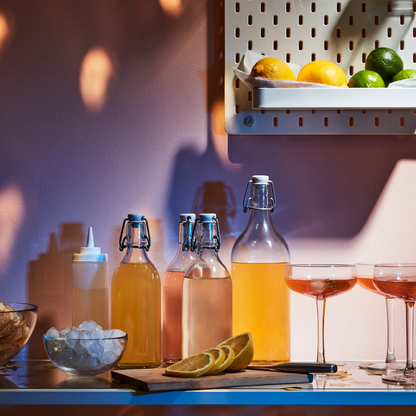 A display of drinks, glasses and accessories on a side table. On the wall above, a SKÅDIS pegboard holds lemons and limes.