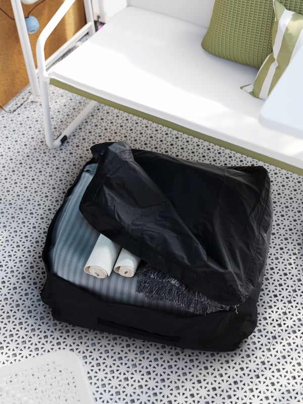 A black storage bag under the sofa, partly unzipped revealing a cushion, rolled placemats, and a throw.