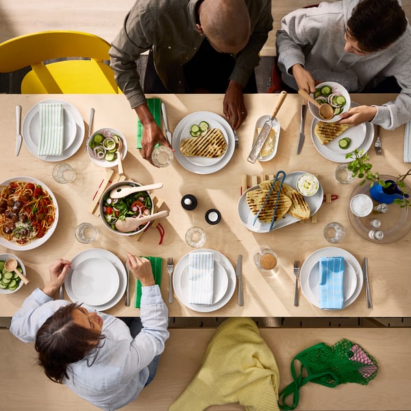 A bird’s-eye view of a BERGSHYTTAN table in birch veneer where people are sharing a meal together on white GODMIDDAG plates.