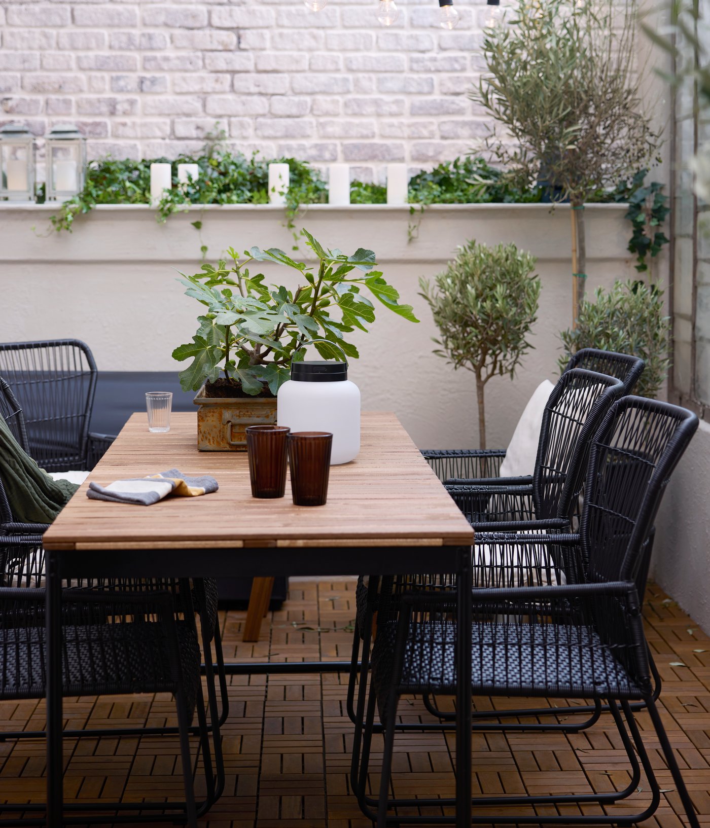 A patio with a VÄSMAN extendable table surrounded by TALLSKÄR chairs with armrests, and a LÄNSPORT portable LED light on it.