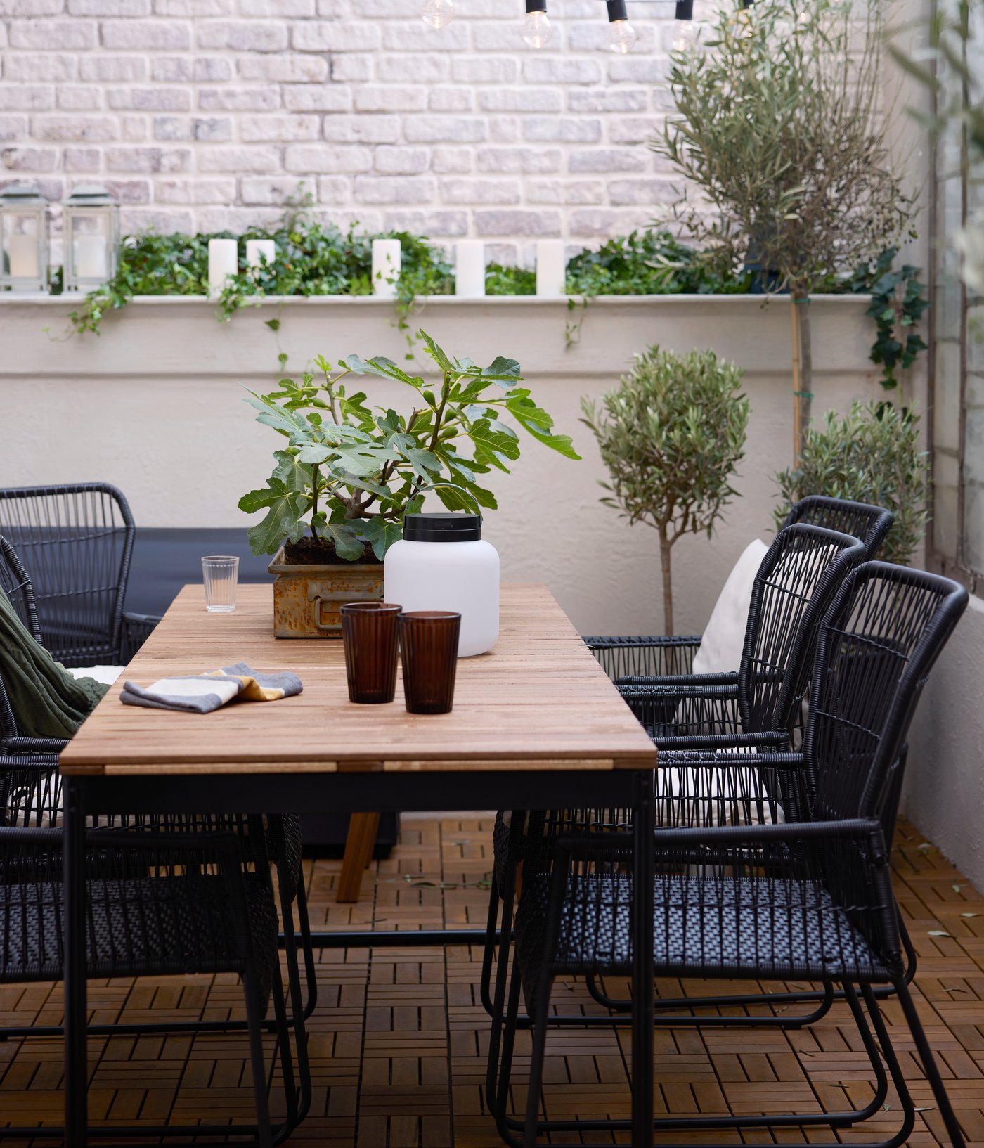 A patio with a VÄSMAN extendable table surrounded by TALLSKÄR chairs with armrests, and a LÄNSPORT portable LED light on it.