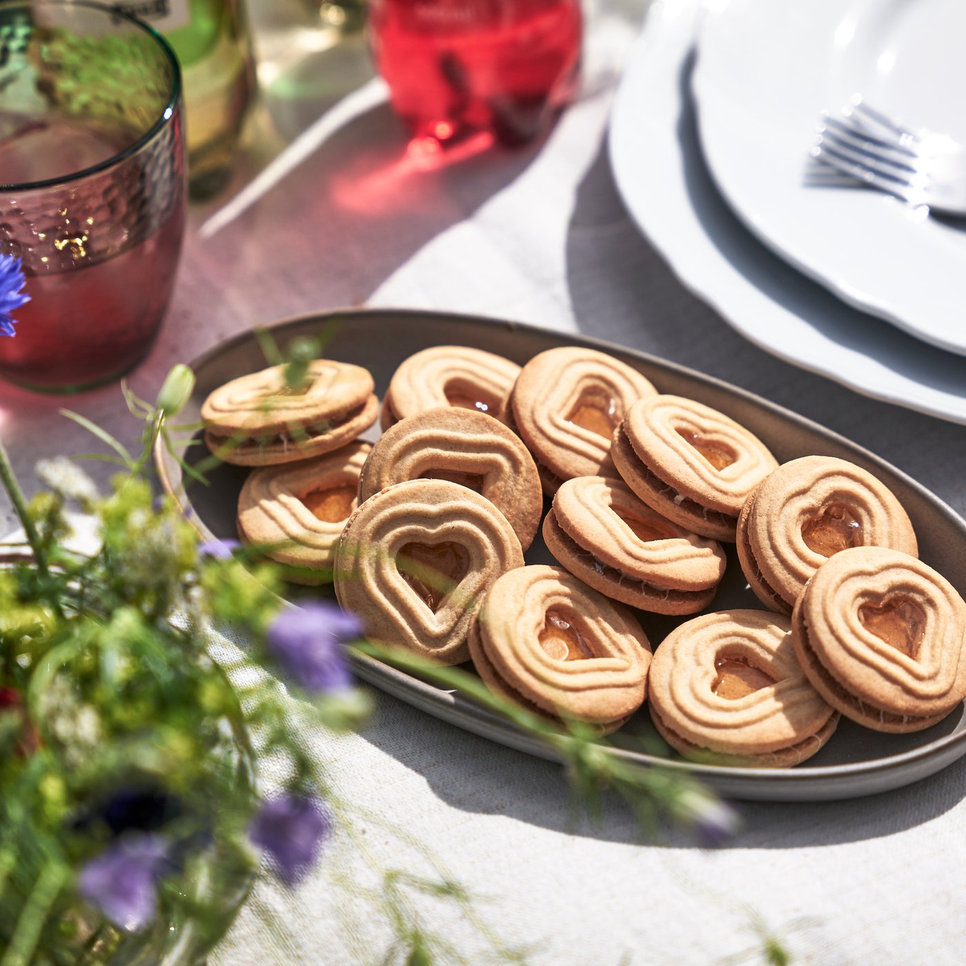 Gedeckter Tisch mit Blumen und einem Servierteller mit Keksen drauf. 