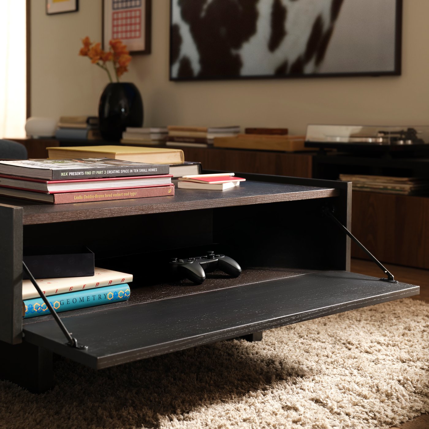 An opened shelf of the TRANERED square coffee table, with game controller inside.