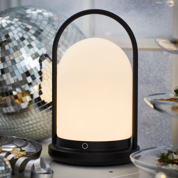 Une lanterne LED FRÖJDA noire pour l'extérieur, alimentée par des piles et dotée d'un variateur de lumière.