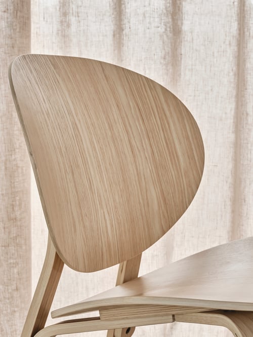 Un salon avec plan rapproché d'un fauteuil en bois beige avec dossier arrondi placé en face d’un mur de couleur neutre.