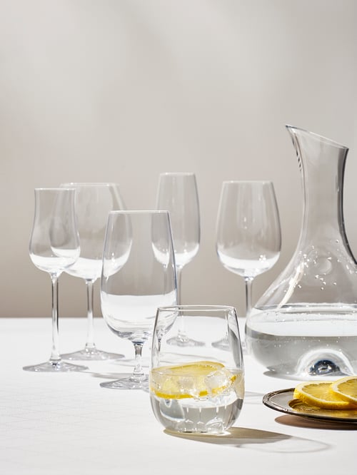 A modern dining room that features a white glass, a dessert wine glass, a champagne glass, a beer glass, and a carafe.