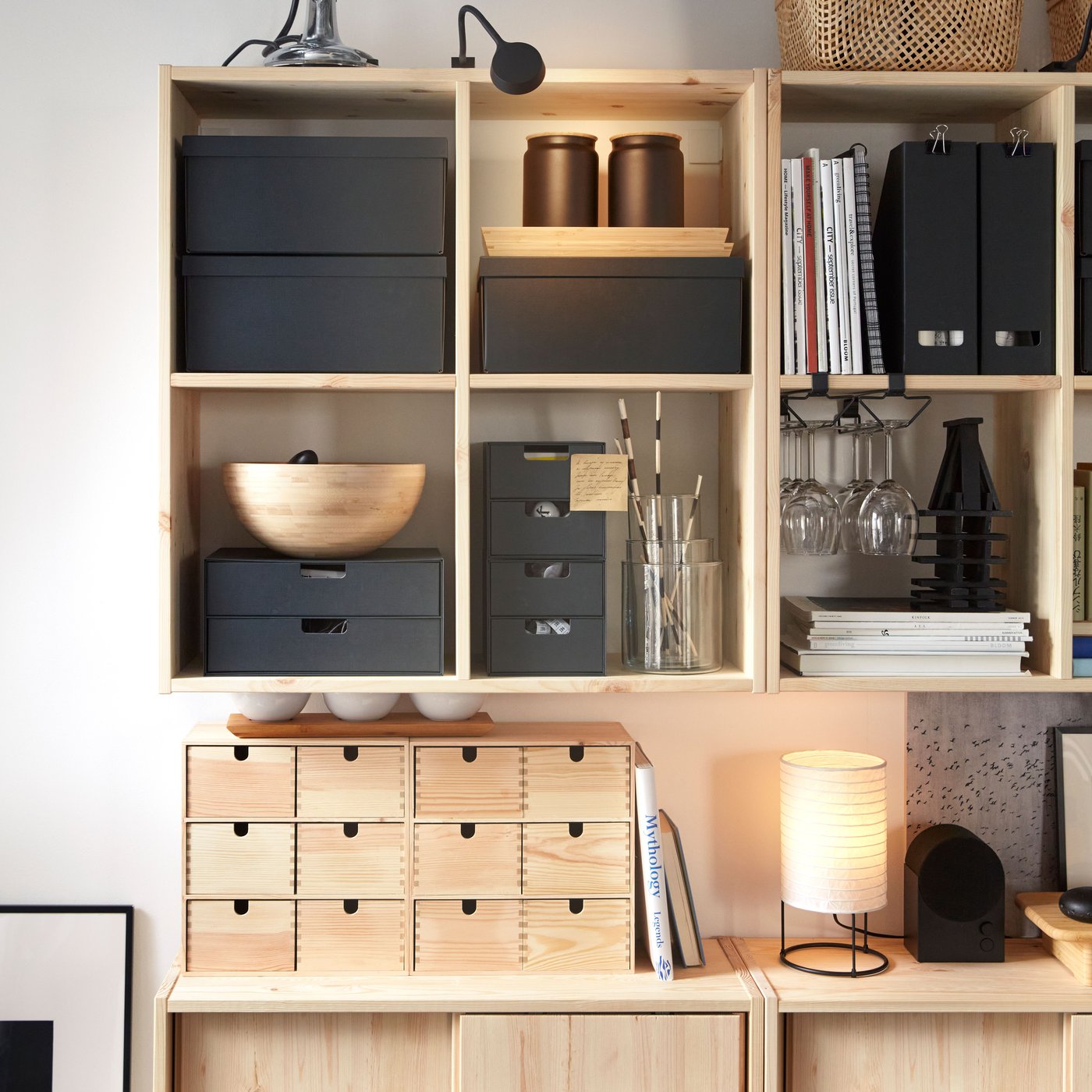 Two IVAR wall shelves in pine holding black storage boxes and other objects, placed above IVAR cabinets with sliding doors.
