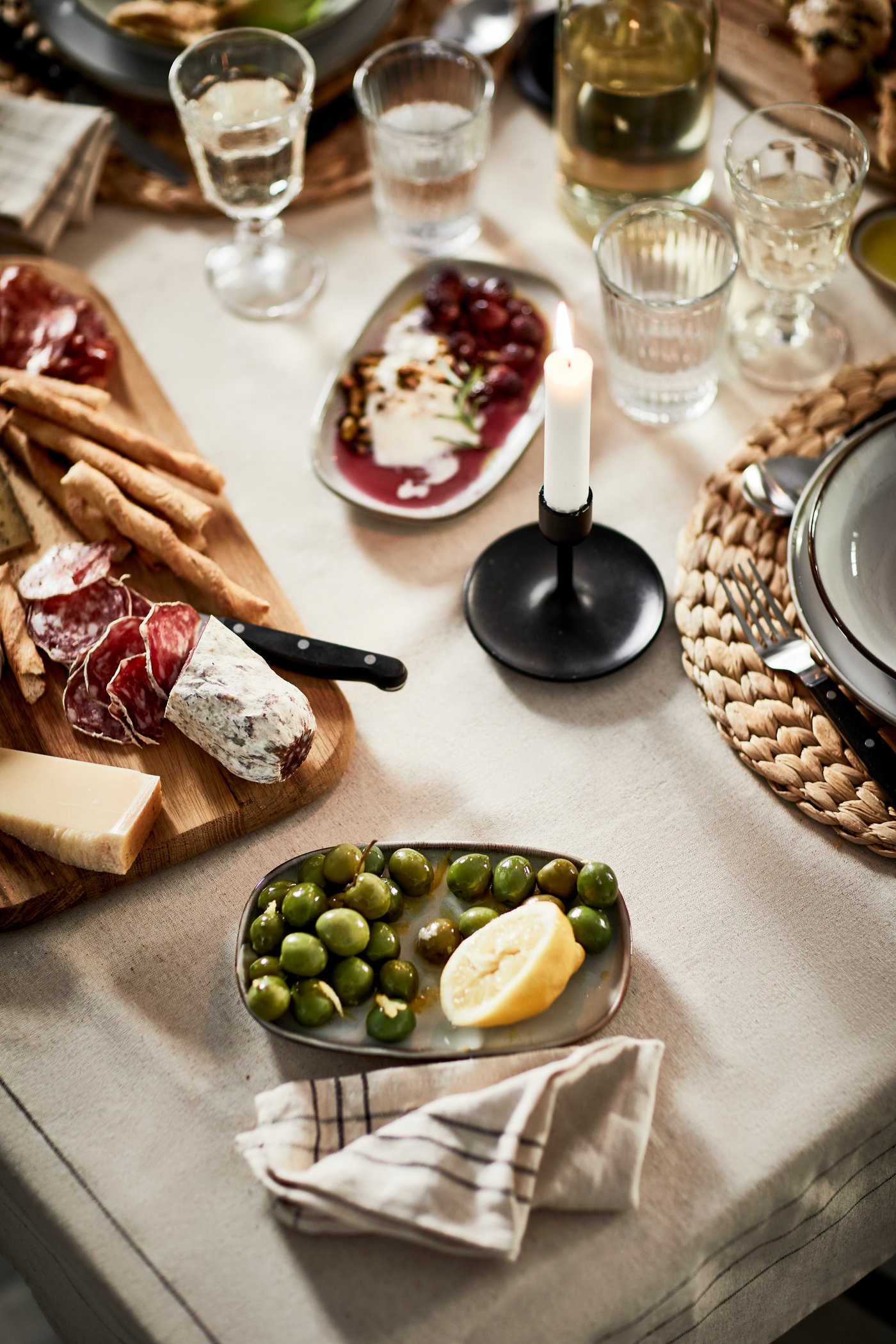 A set dining table filled with tasty bites, including an ARTISTISK snack board with charcuterie, olives, and grape salad.