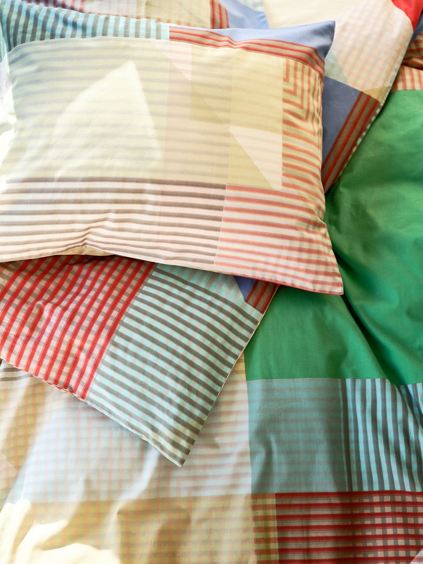 Details of vibrant patterns in reds, yellows, blues and greens on the PIMPERNÖT pillows sprawled on the PIMPERNÖT quilt.