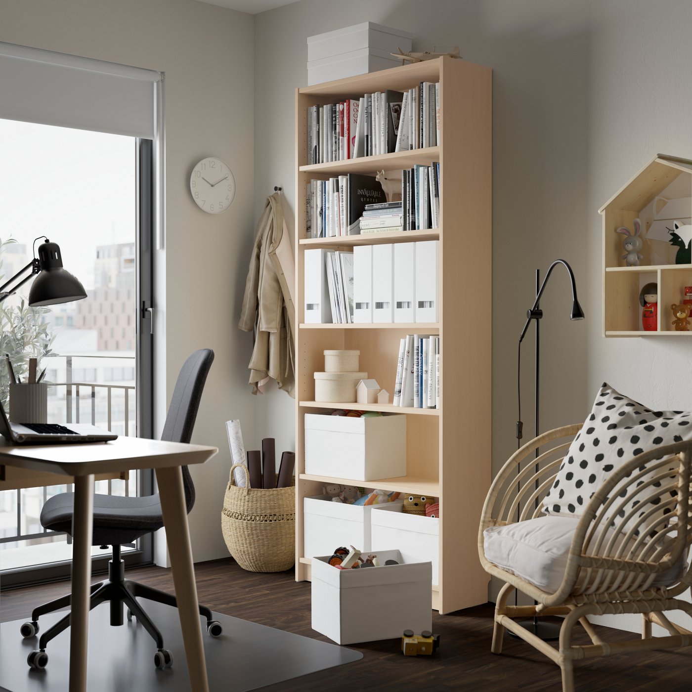 Home office with a tall wood bookshelf, desk by a window, and a rattan chair with a patterned pillow.
