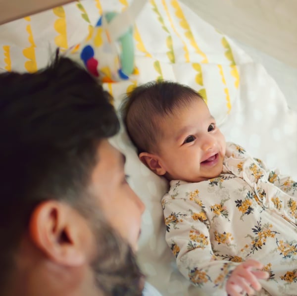 Glad baby og far ligger smilende i en seng.