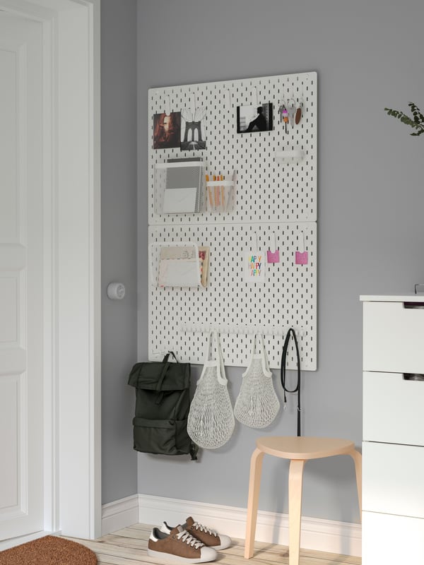 Child putting socks on, seated on a stool. On the wall behind hangs a SKÅDIS pegboard, holding various clothing items.