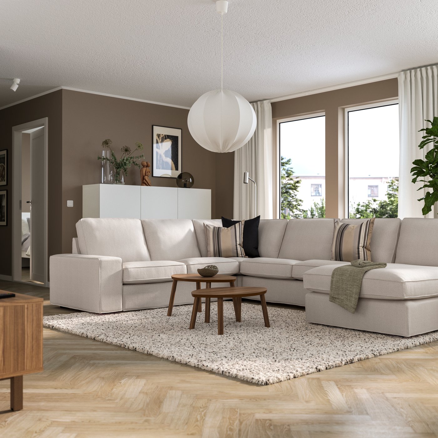Een Japandi woonkamer met een Tresund lichtbeige KIVIK hoekbank, 5-zits met chaise longue met houten salontafels en een hoogpolig vloekleed.