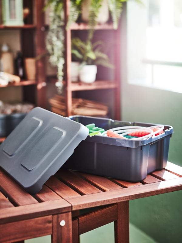 Un contenitore in plastica KLÄMTARE aperto posto con al suo interno alcuni oggetti, posto su un tavolino in legno.