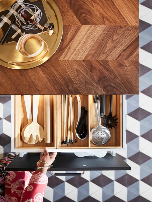 Overhead shot of a custom made worktop with a yellow tray, and an open drawer containing utensils trays with cutlery items.