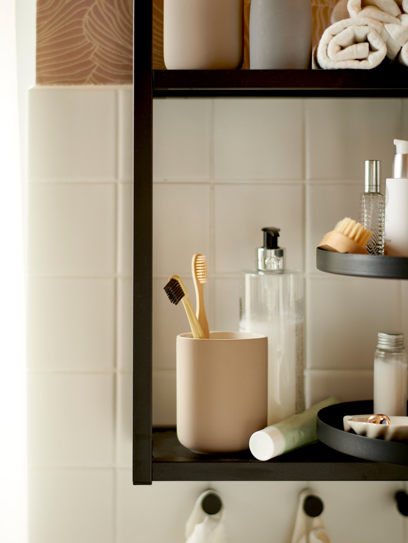 Soporte para cepillos de dientes EKOLN beige sobre un estante ENHET negro, junto a otros artículos de baño y toallas.