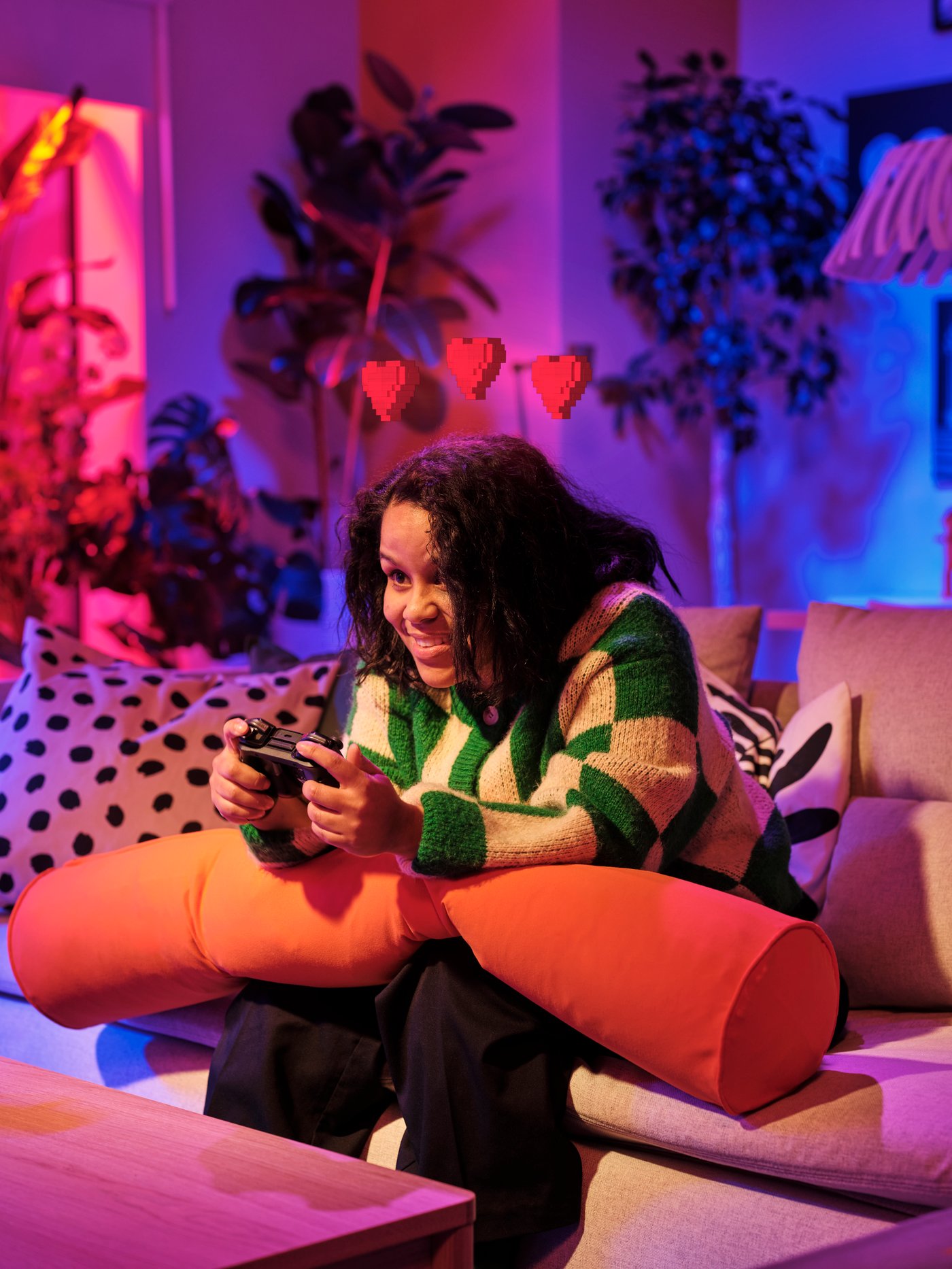 Člověk s herním ovladačem v rukou sedí na pohovce a opírá si ruce o herní polštář BRÄNNBOLL.