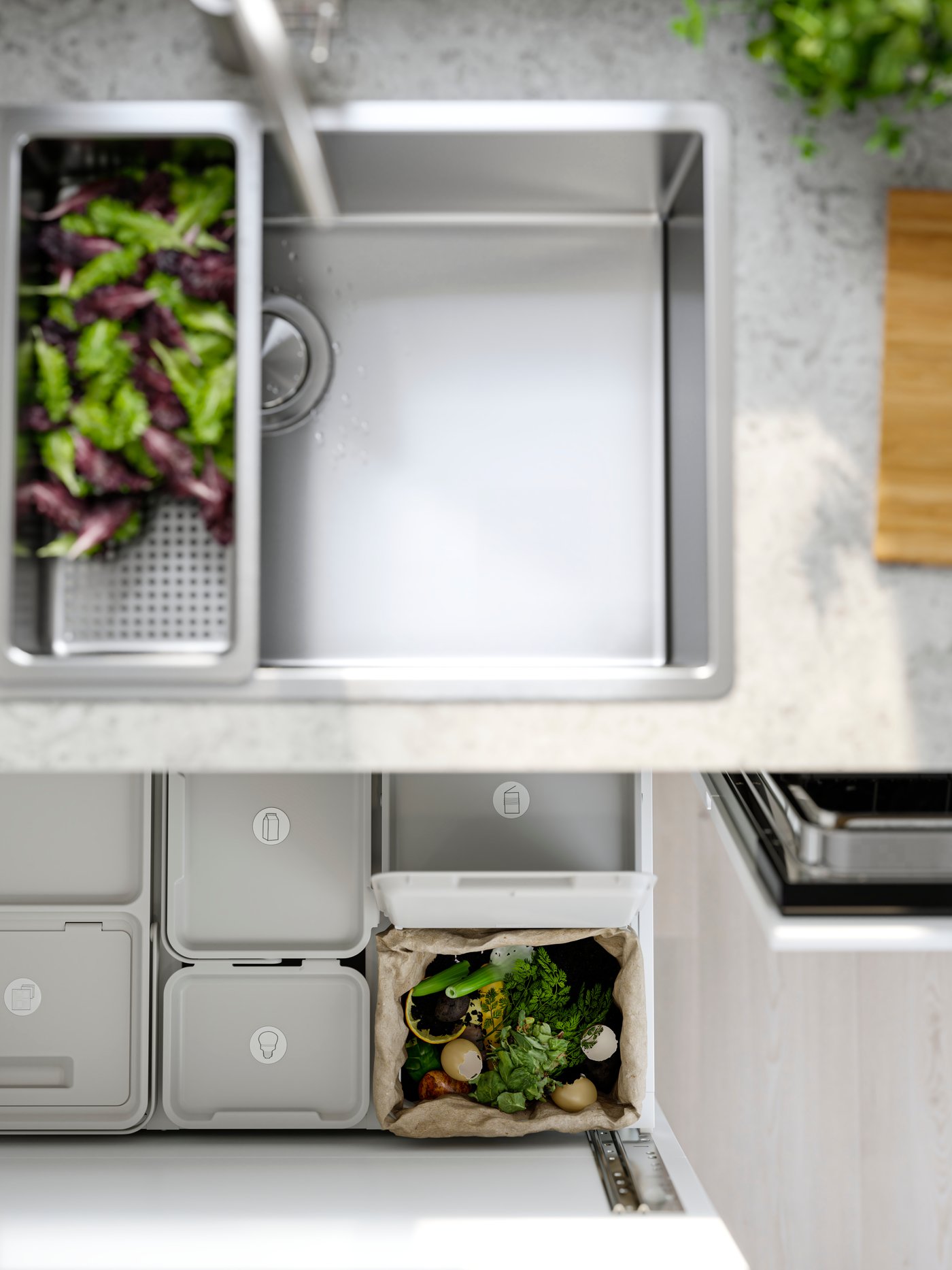 Kuhinjsko korito z odprtim predalom, v katerem so koši za smeti in ločevanje odpadkov.