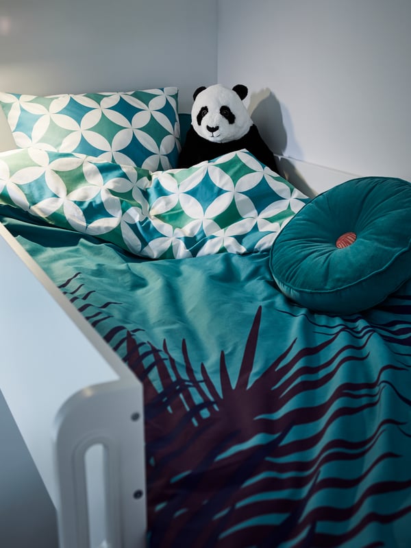 A light pink KRANSBORRE cushion lies on a dark brown stained IDANÄS bed with light pink KRANSKRAGE bed linen.