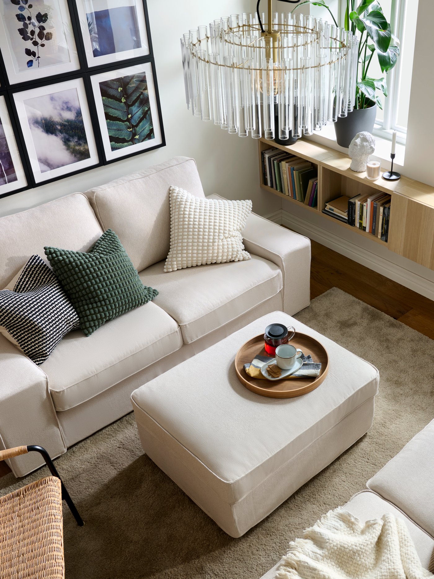A living room with facing KIVIK two-seat sofas with colourful textiles, a pouffe in-between, and neatly arranged wall art.