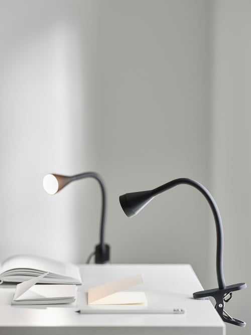 Birou alb cu notebook-uri deschise și două spoturi de prindere cu LED-uri negre din plastic flexibil, cu brațe și capete reglabile.