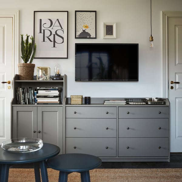 Grey HAUGA cabinets and drawers in a living room below a smart TV and KNOPPANG frames on the wall. 