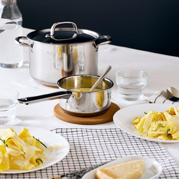 An IKEA 365+ saucepan with lid in stainless steel on HEAT pot stand in cork and an IKEA 365+ pot with lid in stainless steel.