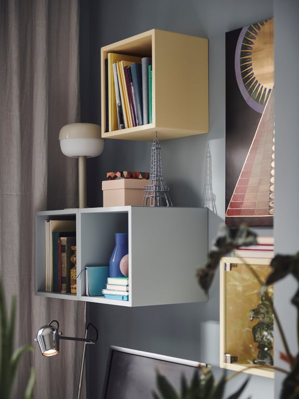 EKET cabinets in blue and yellow, with books and various items, mounted in a whimsical pattern against a blue wall.