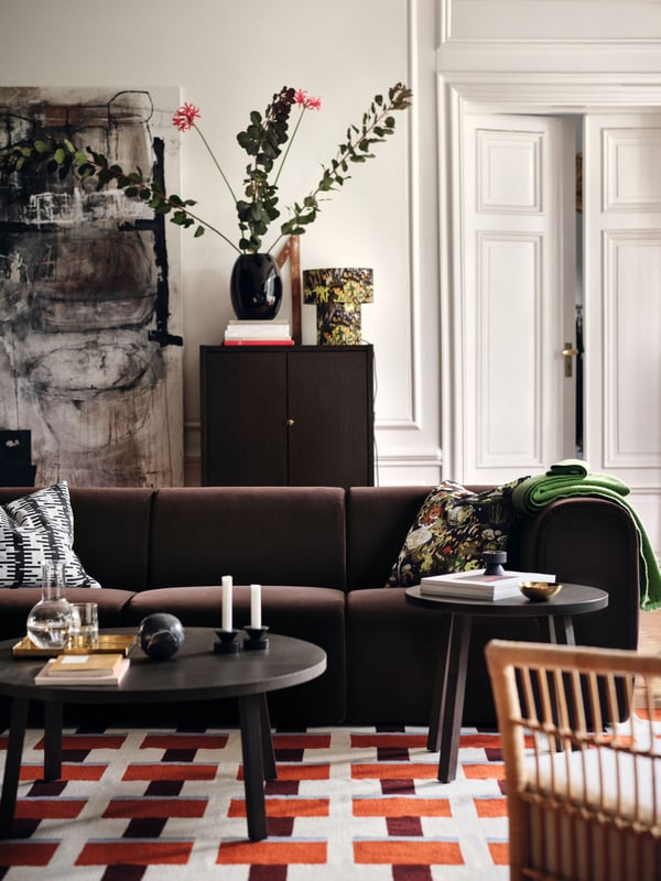 A living room with a dark brown STOCKHOLM 2025 4-seat sofa, tables in front of it, all placed on a patterned, flatwoven rug.