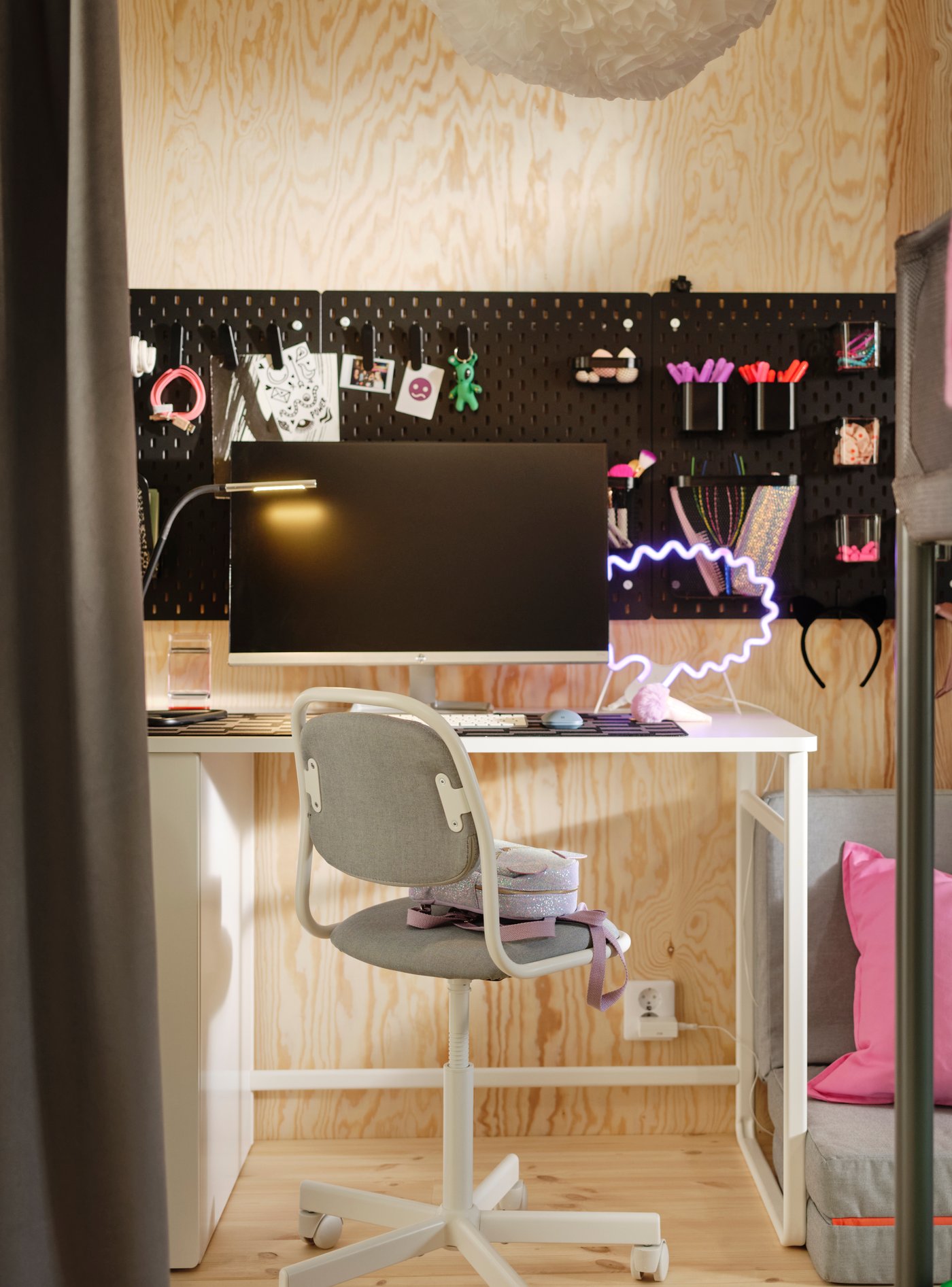 An IKEA white desk with an ÖRFJÄLL child desk chair in light green, on a room with wood wall panels and a blackboard on the wall.