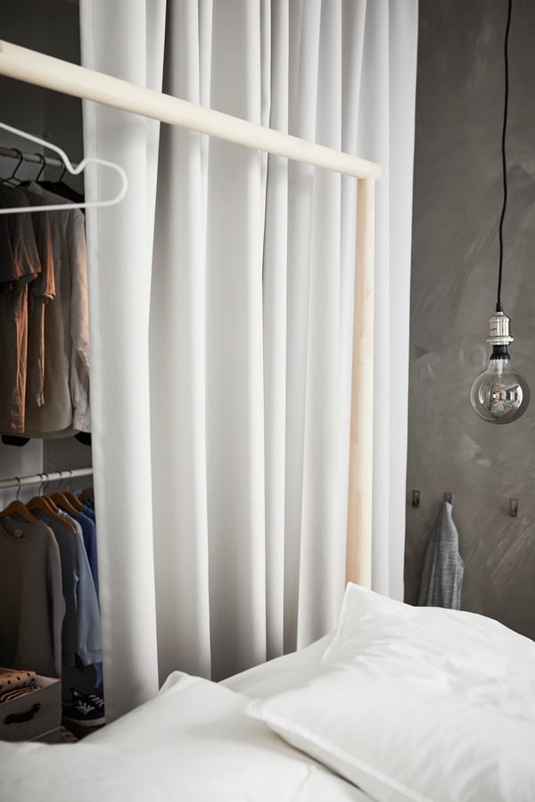 A wardrobe area, with light grey GUNRID curtains around it, contains a black TURBO clothes rack and storage boxes on shelves.
