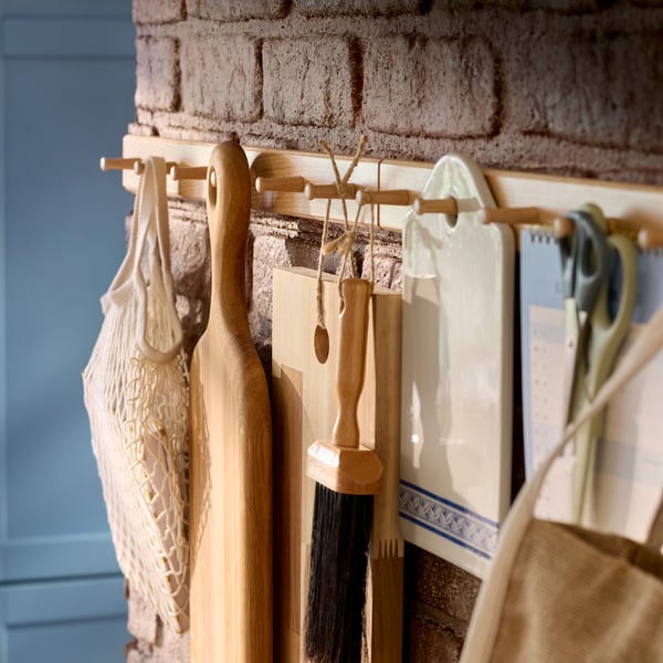 Two HÖVOLM racks with 6 knobs each are mounted on a brick wall and there are different kitchen items hanging from the knobs.
