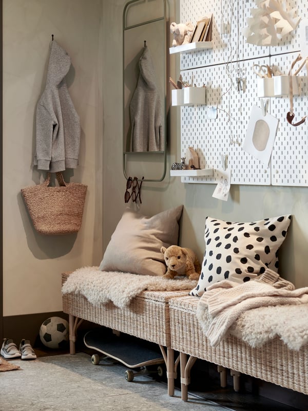 A hallway with two rattan benches with storage inside and cushions and rugs on top, plus white pegboards and a green mirror.