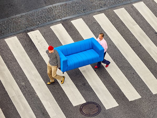Two people carrying a blue KLIPPAN sofa while crossing the street.