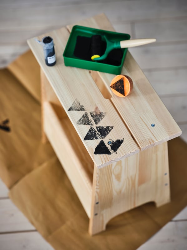 An ongoing session using a carved sweet potato to paint geometric patterns on a PERJOHAN pine bench with storage.