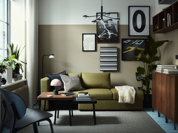 En gul-grøn SKÖNABÄCK sofa i en retroinspireret dagligstue med to SONHULT indskudsborde med valnøddetræsmønster.