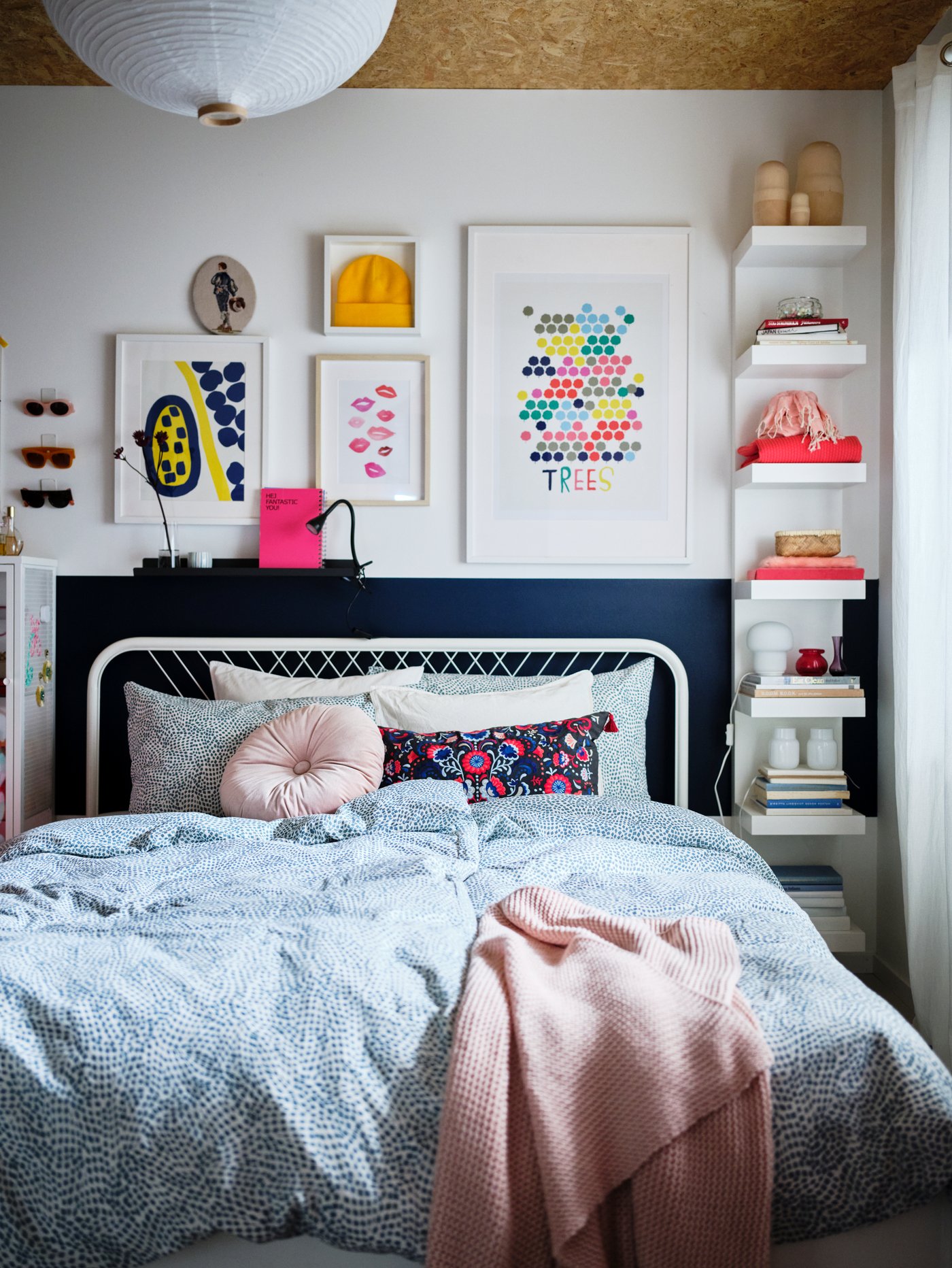 A bedroom in light shades and colourful decorations, and a white NESTTUN bed made with blue-and-white TRÄDKRASSULA bed linen.