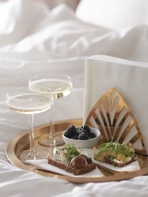 Un gros plan d’un plateau avec un bol de service contenant des fruits, une assiette avec des rôties, des serviettes de table blanches dans un présentoir à serviettes, et des coupes de champagne.
