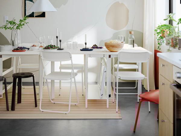 Zwei weiße VIHALS Klapptische bilden eine Tafel, an der verschiedene Stühle der VIHALS Serie und Hocker stehen.