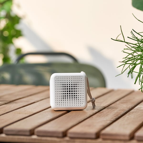 A waterproof white VAPPEBY portable Bluetooth speaker stands on top of a table on a balcony on a sunny day.