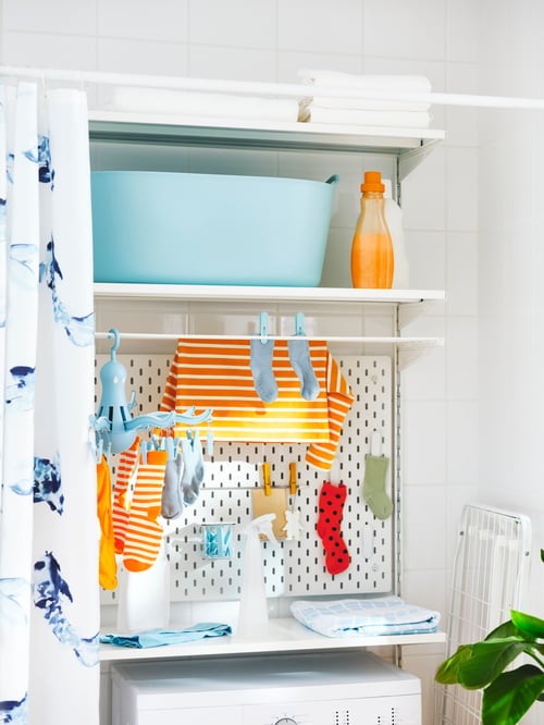 Un coin de buanderie avec un panier à linge flexible TORKIS, un panneau perforé SKÅDIS , un cintre avec des piquets et du linge sur une section BOAXEL.